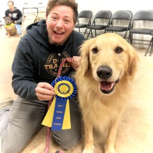 Dog trainer and golden retriever smile with CGC ribbon