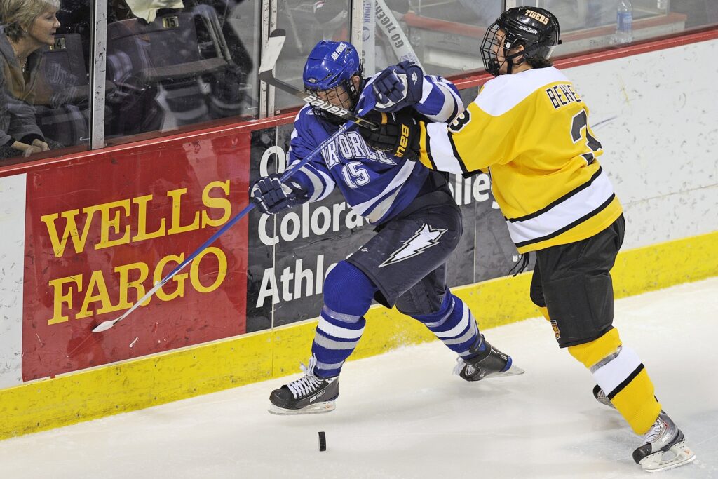 Two hockey players near a wall going for the puck