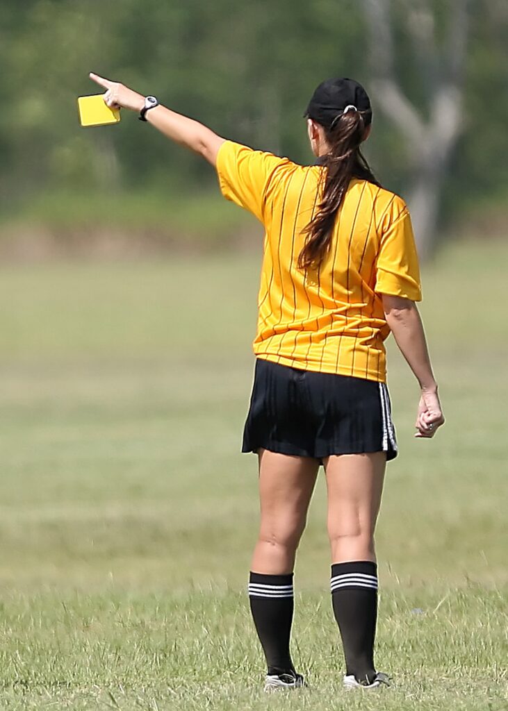 referee stands with back to camera and is pointing with a yellow card in hand