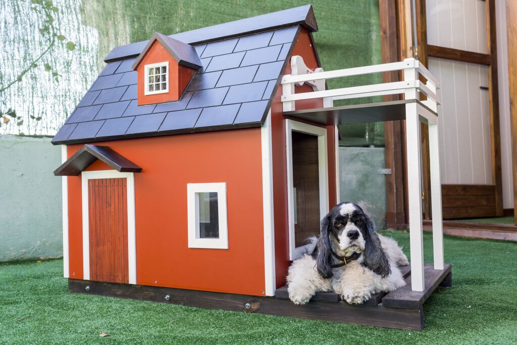 small dog laying on the porch of a dog house made to look like a barn